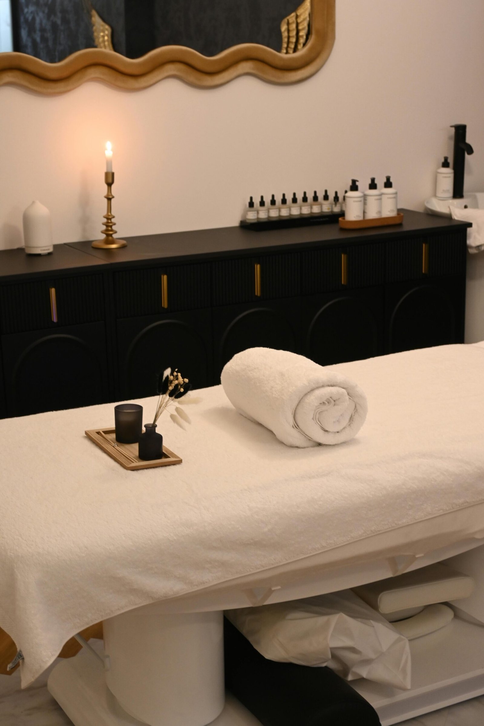 Elegant spa room with rolled towel, candle, and essential oils on massage table.
